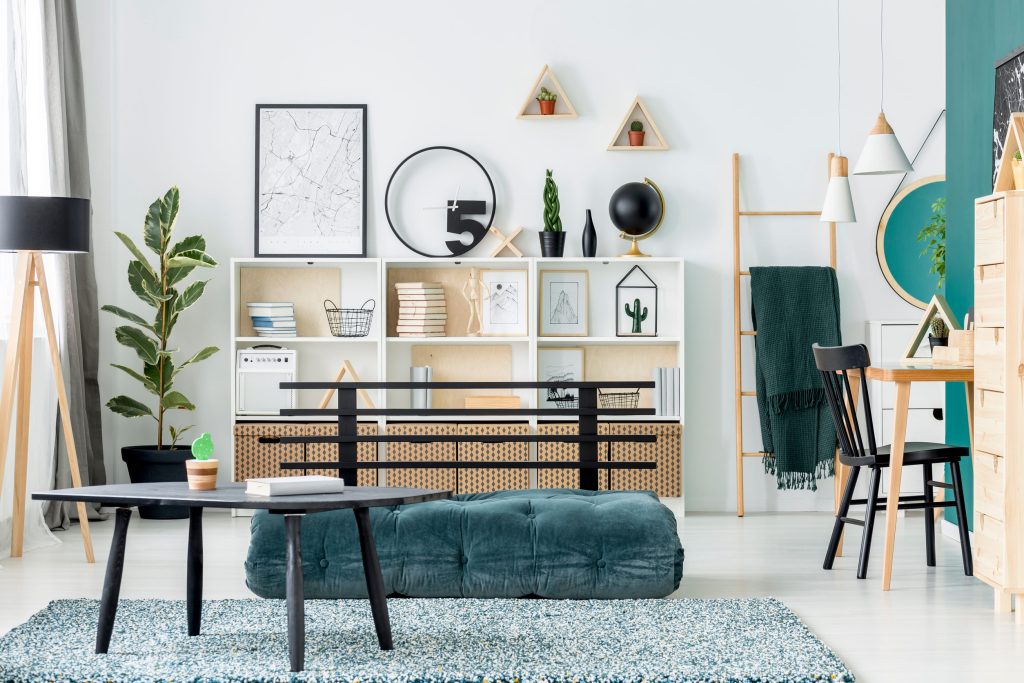 Bright modern living room with a white shelving unit, teal tufted bench, black coffee table, and a tall plant near a window.