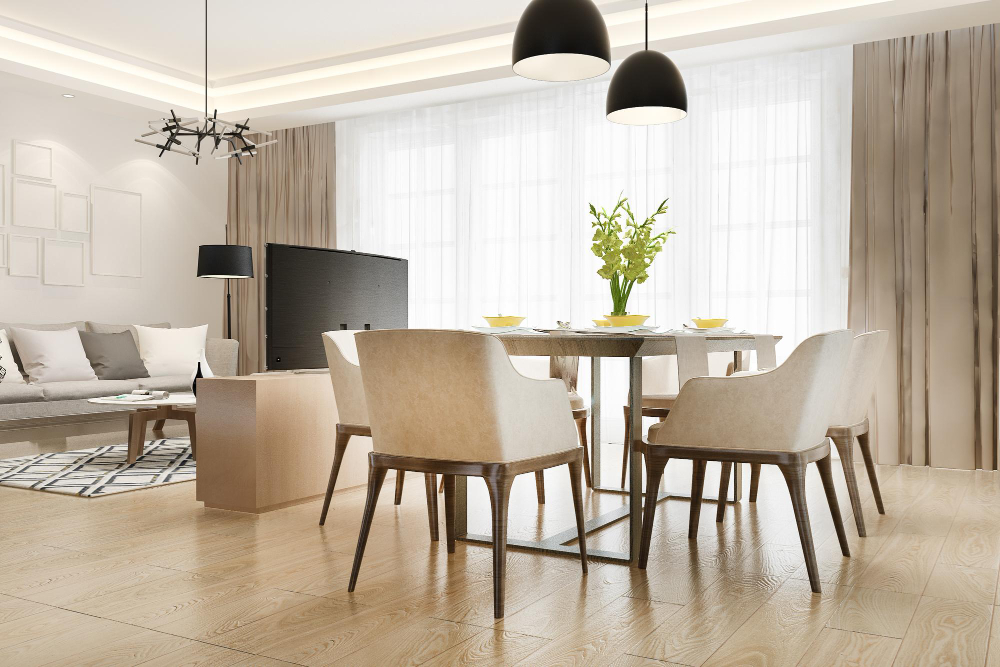 Open-concept living and dining area with a wooden dining table, beige chairs, tall windows with sheer curtains, and modern black pendant lights above the table.