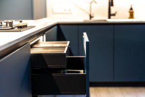 Blue kitchen island with open drawers showing storage and trays; stove on left and sink area in the background.