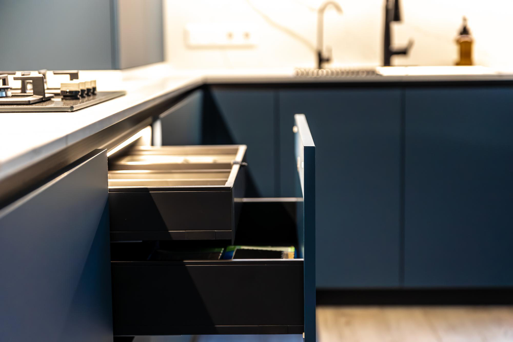 Blue kitchen island with open drawers showing storage and trays; stove on left and sink area in the background.