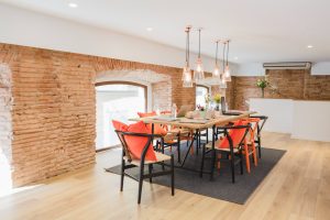 775522 - Soil Group - Decorar.org Bright coworking space with exposed brick walls, a long wooden table, orange cushions, and glass pendant lights with plants nearby.