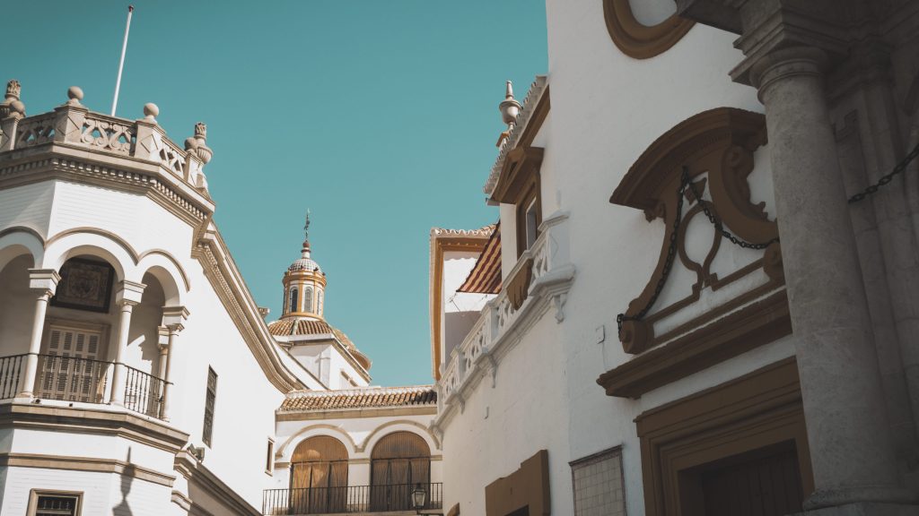 Sunlit white Andalusian buildings with arches and a domed tower against a turquoise sky